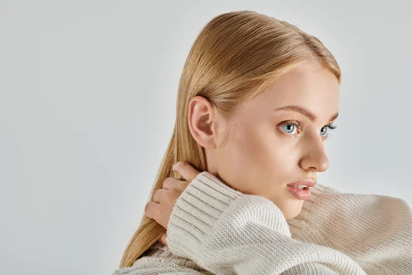 Faszinierende Frau in weißem Strickpullover und natürlichem Make-up mit blonden Haaren auf grauem Hintergrund, Porträt — Stockfoto