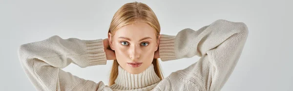 Blondine im Winterpullover posiert mit den Händen hinter dem Kopf und blickt in die Kamera auf grauem Banner — Stockfoto