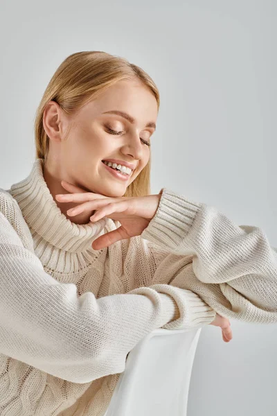 Freudige Frau im weißen warmen Pullover sitzt und lächelt mit geschlossenen Augen auf grauer, winterlicher Stimmung — Stockfoto