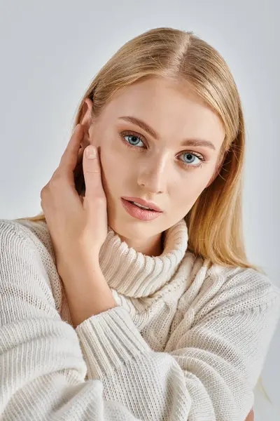 Portrait of sensual blonde woman in natural makeup and white winter sweater touching face on grey — Stock Photo