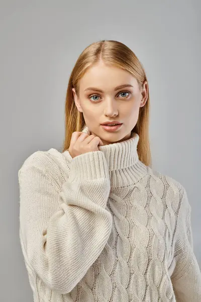 Portrait of blonde woman in white knitted sweater and natural makeup looking at camera on grey — Stock Photo