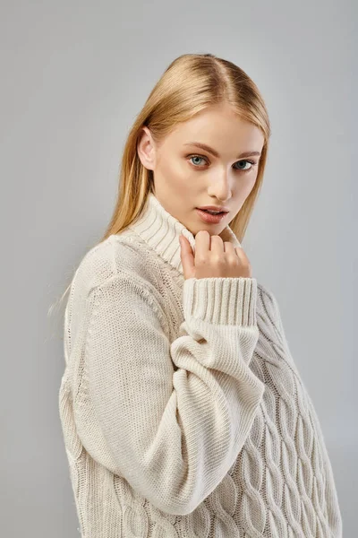 Alluring woman with blonde hair and natural makeup wearing white sweater looking at camera on grey — Stock Photo