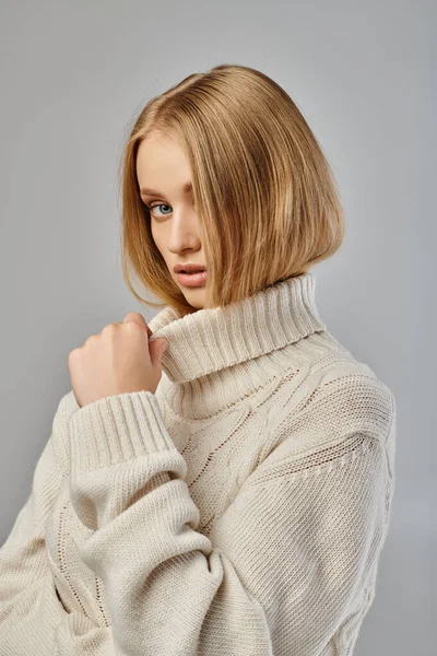 Beautiful blonde woman in white winter sweater looking at camera on grey, sophisticated beauty — Stock Photo