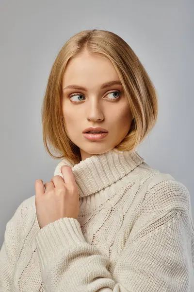 Femme blonde réfléchie en chandail tricoté délicat et confortable regardant loin sur gris, émotions hivernales — Photo de stock