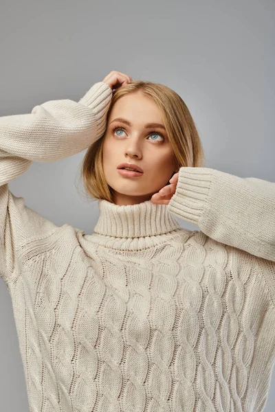 Romantic and dreamy blonde woman in white warm sweater looking away on grey, winter atmosphere — Stock Photo