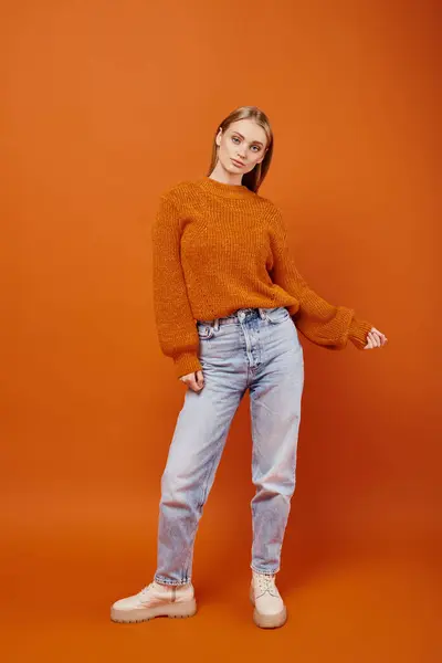 Mujer rubia de moda en jeans y suéter de punto naranja posando sobre fondo brillante, vibraciones de invierno - foto de stock