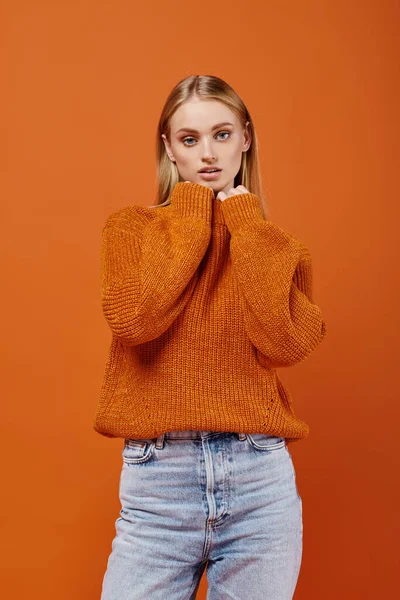 Attractive blonde woman in bright winter sweater and jeans on orange backdrop, street style — Stock Photo