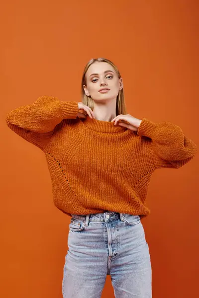 Stylish blonde woman in warm and bright  knitted sweater and blue jeans on orange backdrop, fashion — Stock Photo