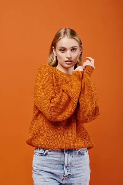 Молодая блондинка в оранжевом трикотажном свитере смотрит в камеру на ярком фоне, зимний тренд — стоковое фото