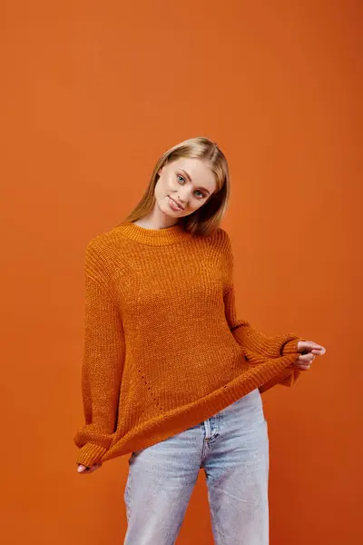 Encantadora mujer rubia estirando su suéter de punto y sonriendo en naranja, emociones de invierno - foto de stock