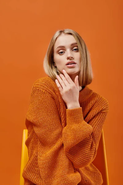 Charming blonde woman in orange sweater sitting on chair and looking at camera on colorful backdrop — Stock Photo