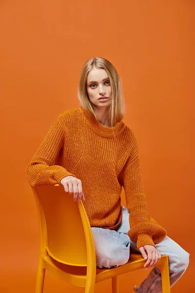 Jolie femme blonde en pull orange tendance assis et regardant la caméra sur fond coloré — Photo de stock