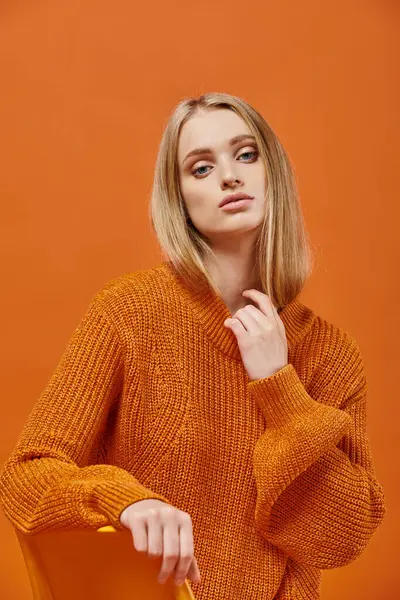 Изысканная блондинка в оранжевом свитере сидит и смотрит в камеру на красочном фоне — стоковое фото