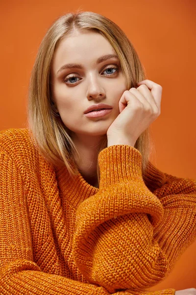 Ritratto di giovane donna in maglione colorato lavorato a maglia con capelli biondi e trucco naturale su arancione — Foto stock