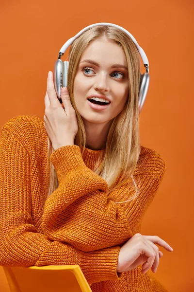Amazed woman in bright warm sweater listening music in headphones on orange, winter emotions — Stock Photo