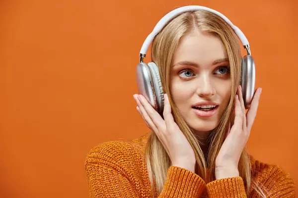 Impressed woman in warm knitted sweater listening music in headphones on orange, winter emotions — Stock Photo
