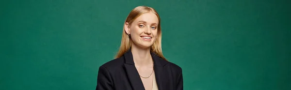 Femme blonde joyeuse et élégante en manteau chaud noir regardant la caméra sur la bannière verte et horizontale — Photo de stock