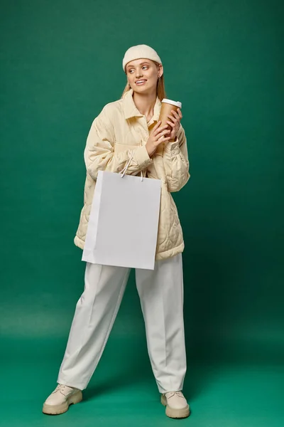 Giovane donna sorridente in abiti invernali alla moda con shopping bag e caffè per andare sullo sfondo verde — Foto stock