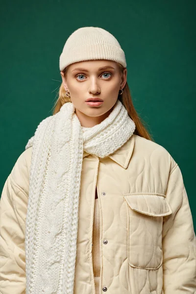 Giovane donna in calda giacca alla moda e sciarpa lavorata a maglia con cappello beanie su sfondo verde, stile invernale — Foto stock