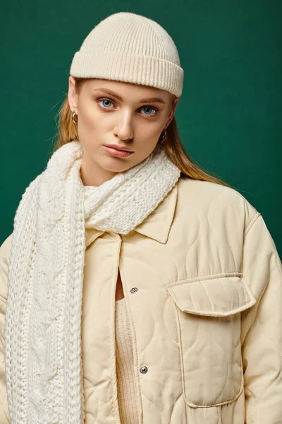 Young woman in ivory jacket and knitted scarf with beanie hat on green backdrop, winter street style — Stock Photo