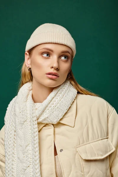 Giovane donna in giacca invernale e sciarpa in maglia con cappello beanie guardando lontano sullo sfondo verde — Foto stock