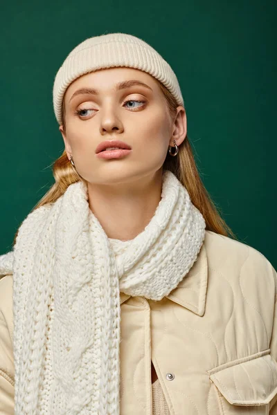 Dreamy woman in trendy jacket and white scarf with beanie hat on green backdrop, winter street style — Stock Photo