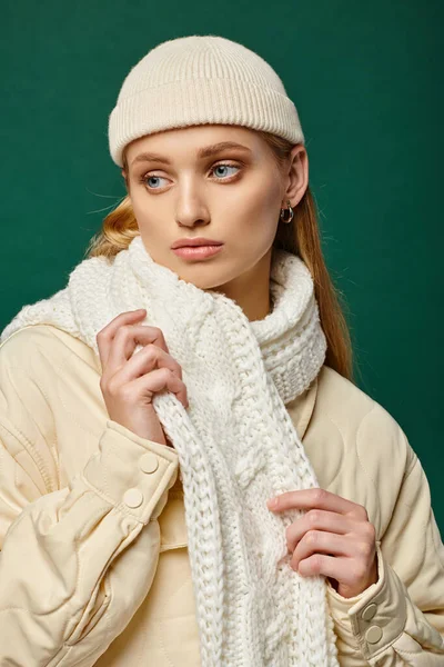 Donna pensosa in giacca calda e sciarpa bianca con cappello beanie su sfondo verde, moda invernale — Foto stock