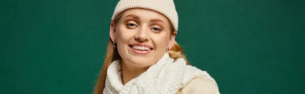 Модна жінка в білому в'язаному шарфі і капелюсі, посміхаючись на камеру на зеленому, зимовому банері — стокове фото