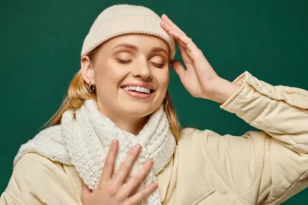 Gioiosa donna in giacca invernale e sciarpa lavorata a maglia con cappello beanie sorridente ad occhi chiusi sul verde — Foto stock