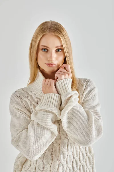 Sensual mujer rubia en suéter de punto blanco mirando a la cámara en gris, moda de invierno - foto de stock