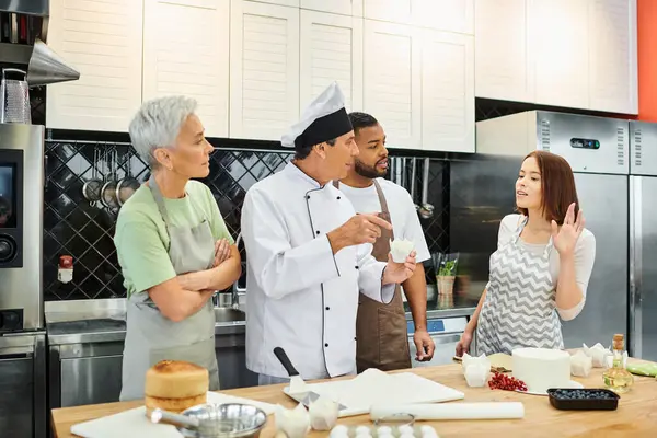 Молода жінка в фартусі поруч зі своїми мультикультурними друзями, які піднімають руку, щоб запитати шеф-кухаря, кулінарні курси — стокове фото