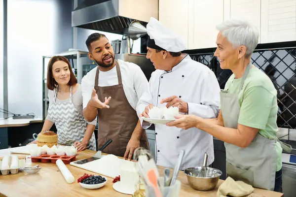 Alegres personas multirraciales en delantales hablando con el chef maduro en sombrero blanco, cursos de cocina - foto de stock