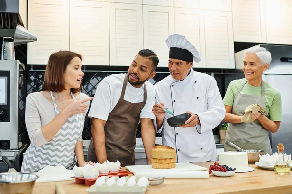 Personnes multiraciales gaies dans des tabliers discuter de la façon de cuisiner avec un chef mature pendant la leçon — Photo de stock