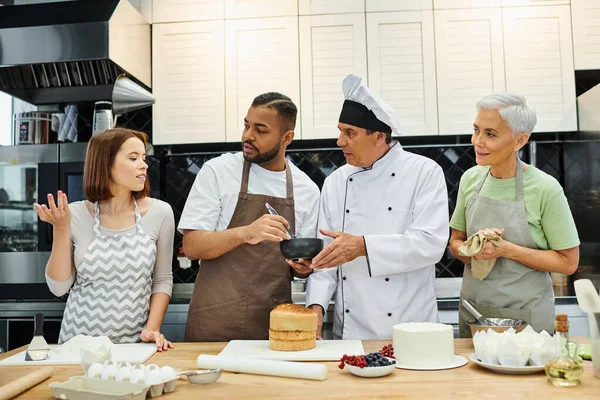 Attractive diverse students and mature chef looking at young woman asking question, cooking courses — Stock Photo