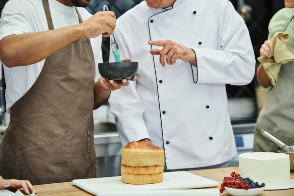 Cropped view of young african american man brushing cake with syrup next to chef and his friends — Stock Photo