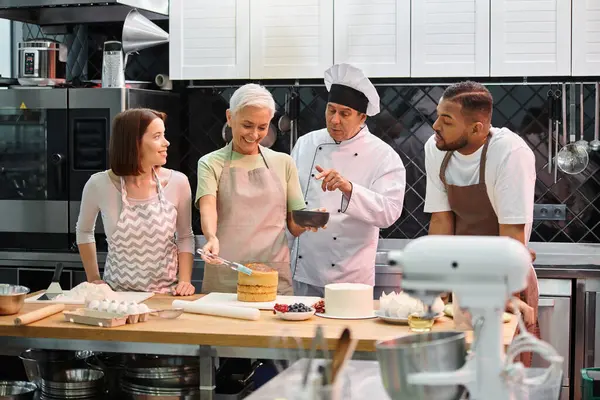 Chef explaining how to use silicone brush on cake to his mature student next to her diverse friends — Stock Photo