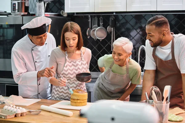 Jolly diverse students watching how chef teaching their young friend how to use silicone brush — Stock Photo