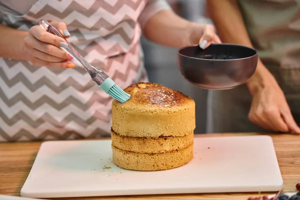 Junge Frau mit Schürze Bürstenkuchen mit Sirup auf leckeren Kuchen während des Kochkurses, Kurse — Stockfoto