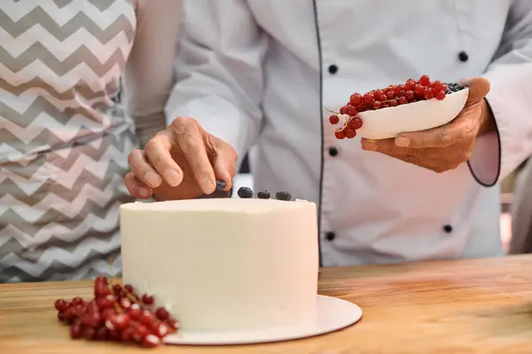 Vue recadrée du chef mature décorer gâteau avec des baies à côté de son jeune étudiant, cours de cuisine — Photo de stock