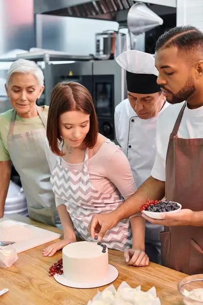 Bello afroamericano uomo decorazione torta accanto ai suoi amici attraenti e chef in cappello bianco — Foto stock