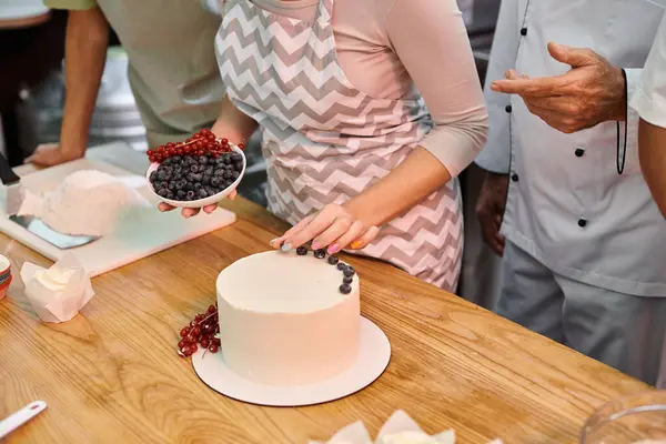 Abgeschnittene Ansicht einer jungen Frau, die neben ihrem reifen Freund und Koch Kuchen mit Beeren dekoriert — Stockfoto