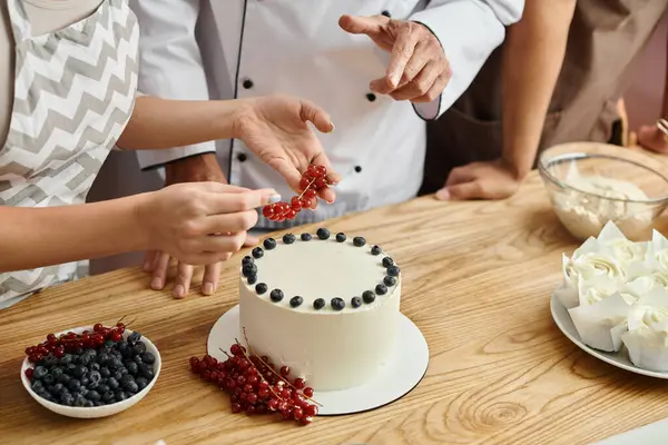 Vue recadrée de jeune femme décorant gâteau avec groseille rouge près du chef et ami afro-américain — Photo de stock