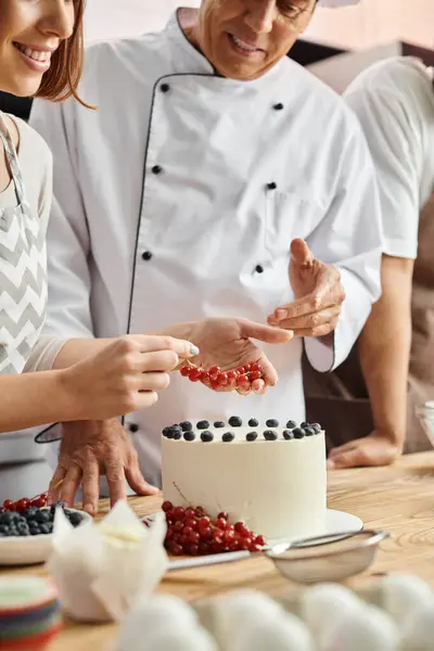 Обрізаний вид на веселу молоду жінку, що прикрашає торт біля зрілого шеф-кухаря та її афроамериканського друга — стокове фото