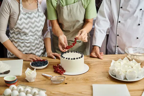 Vue recadrée de femme mature décoration gâteau avec des baies à côté du chef et son jeune ami — Photo de stock