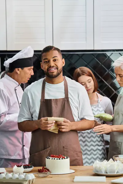 Focus sur l'homme afro-américain joyeux avec gâteau souriant à la caméra avec ses amis flous sur fond — Photo de stock