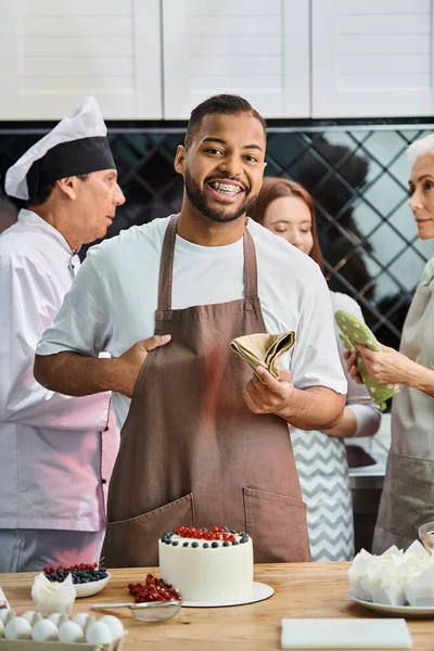 Concentrarsi su jolly africano americano uomo sorridente alla macchina fotografica con i suoi amici offuscati e chef sullo sfondo — Foto stock