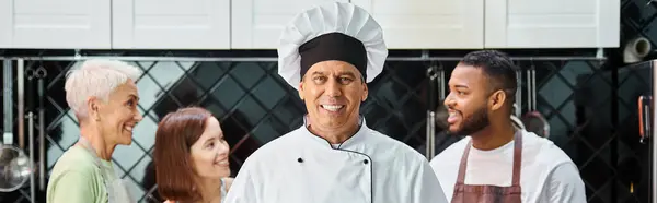 Focus on happy chef with cake smiling at camera with his blurred students on backdrop, banner — Stock Photo