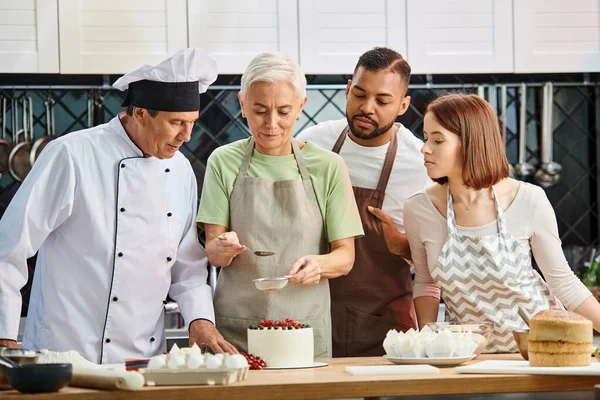 Reife Frau in Schürze dekoriert Kuchen vor Koch und ihren vielfältigen Freunden, Kochkurse — Stockfoto