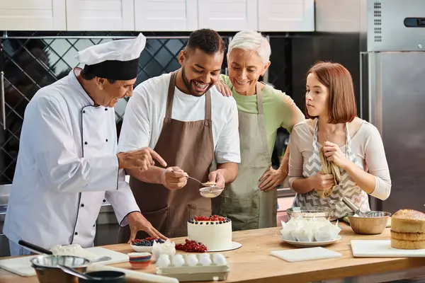 Веселий зрілий шеф-кухар посміхається на його афроамериканський студент прикрашає торт поруч зі своїми друзями — стокове фото