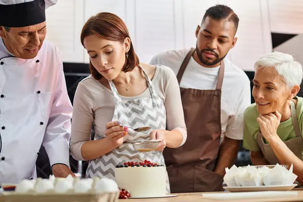 Fröhliche Koch und seine interracial Studenten beobachten junge Frau beim Dekorieren von Kuchen, Kochkurse — Stockfoto